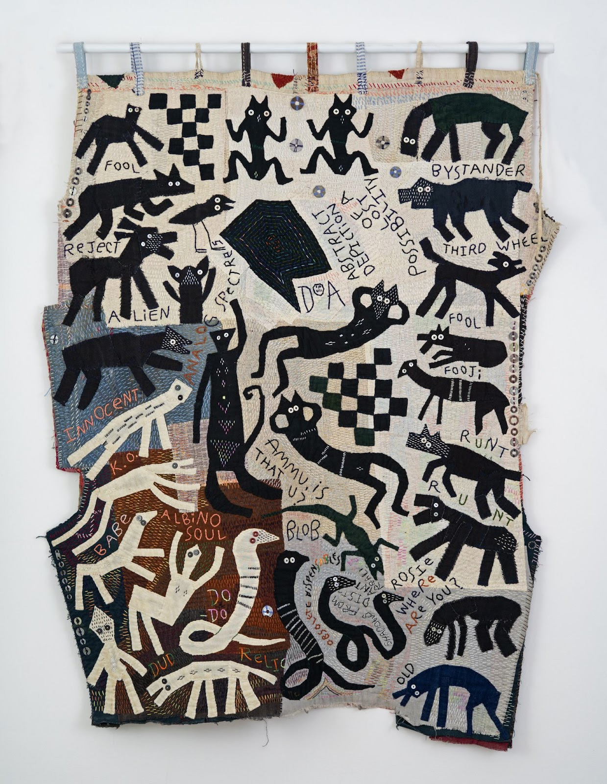 A tapestry with elements of text, animal silhouettes and chequered patterns stitched in tones of black, cream, grey and brown.