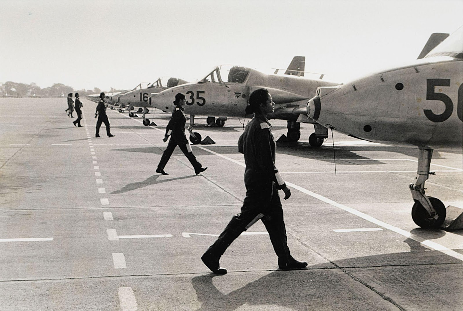 A black and white photograph of a series of uniformed female pilots march towards their individual jets waiting on the tarmac.